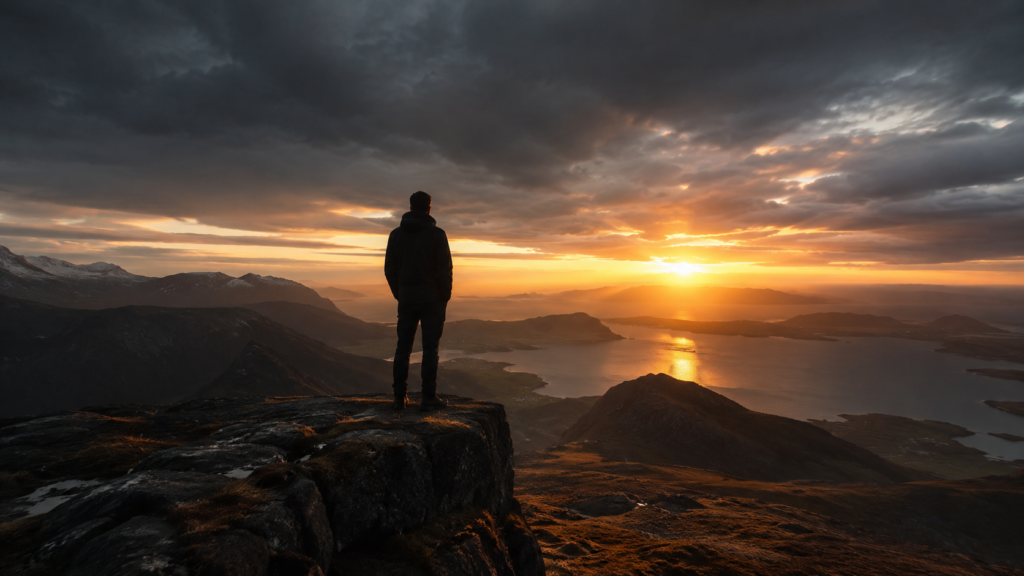 Man standing alone at the edge of a cliff at dawn, looking ahead with calm focus under a dark cinematic sky.