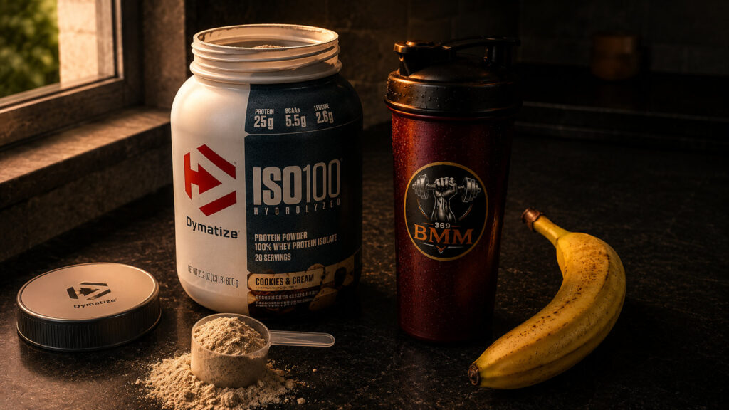 Dymatize ISO100 protein tub with BMM369 shaker and banana on dark counter with warm moody lighting