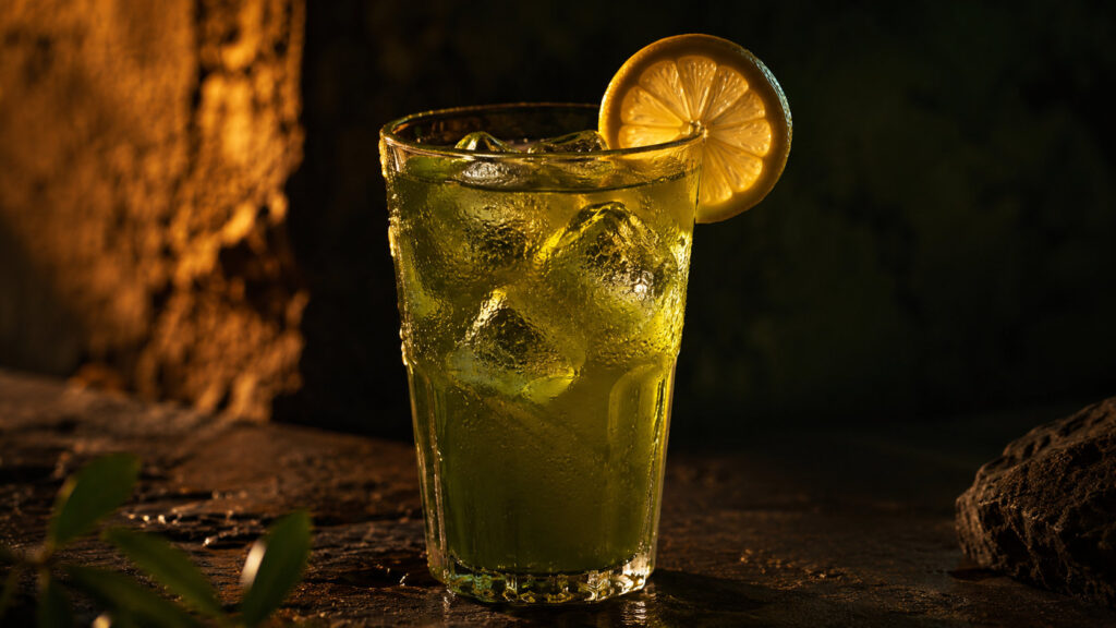 Tall glass of iced green tea with lemon and honey on dark stone surface with orange lighting